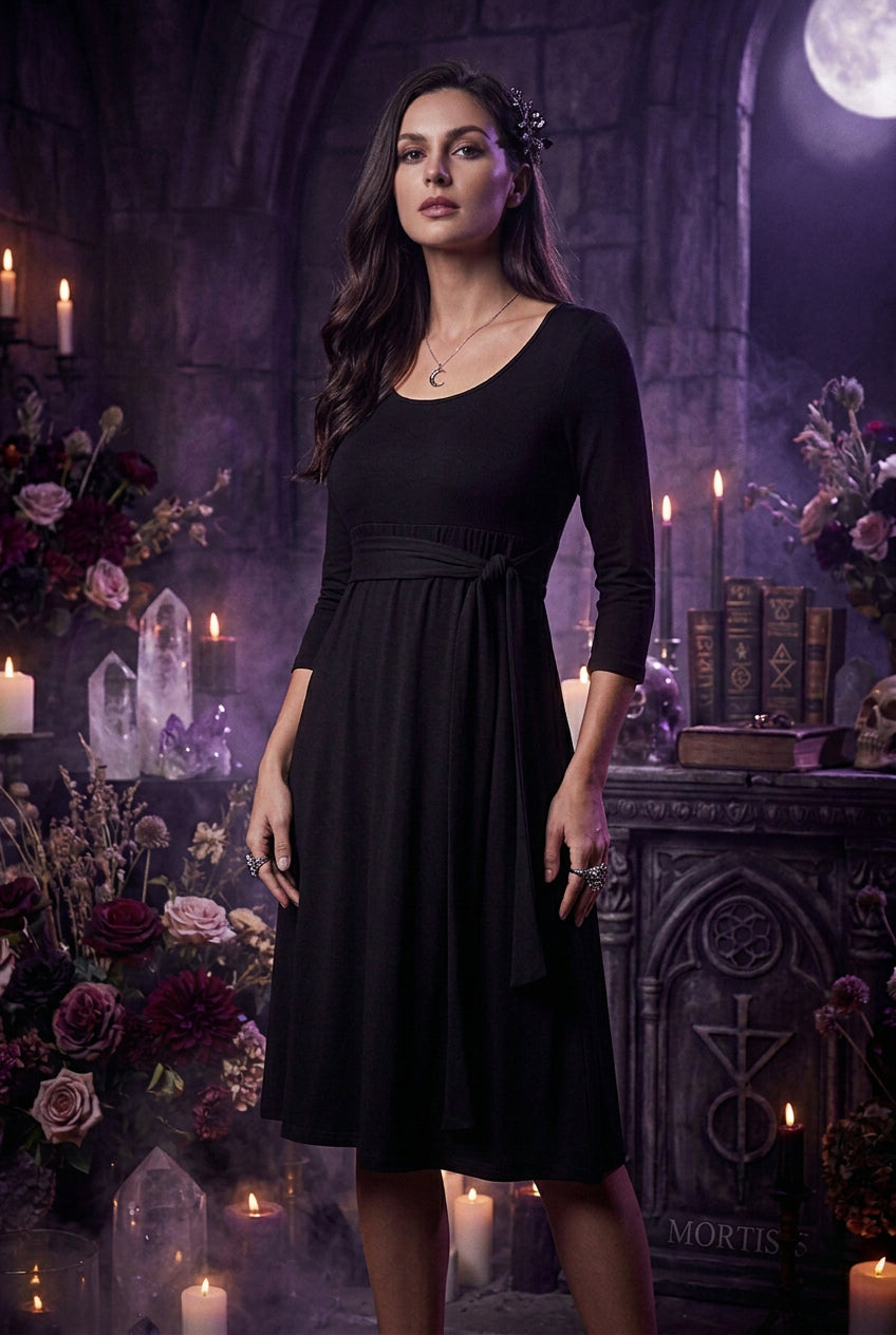A woman wearing a black three-quarter sleeve dress with a scoop neckline and a matching fabric tie belt at the waist, shown against a plain white background.
