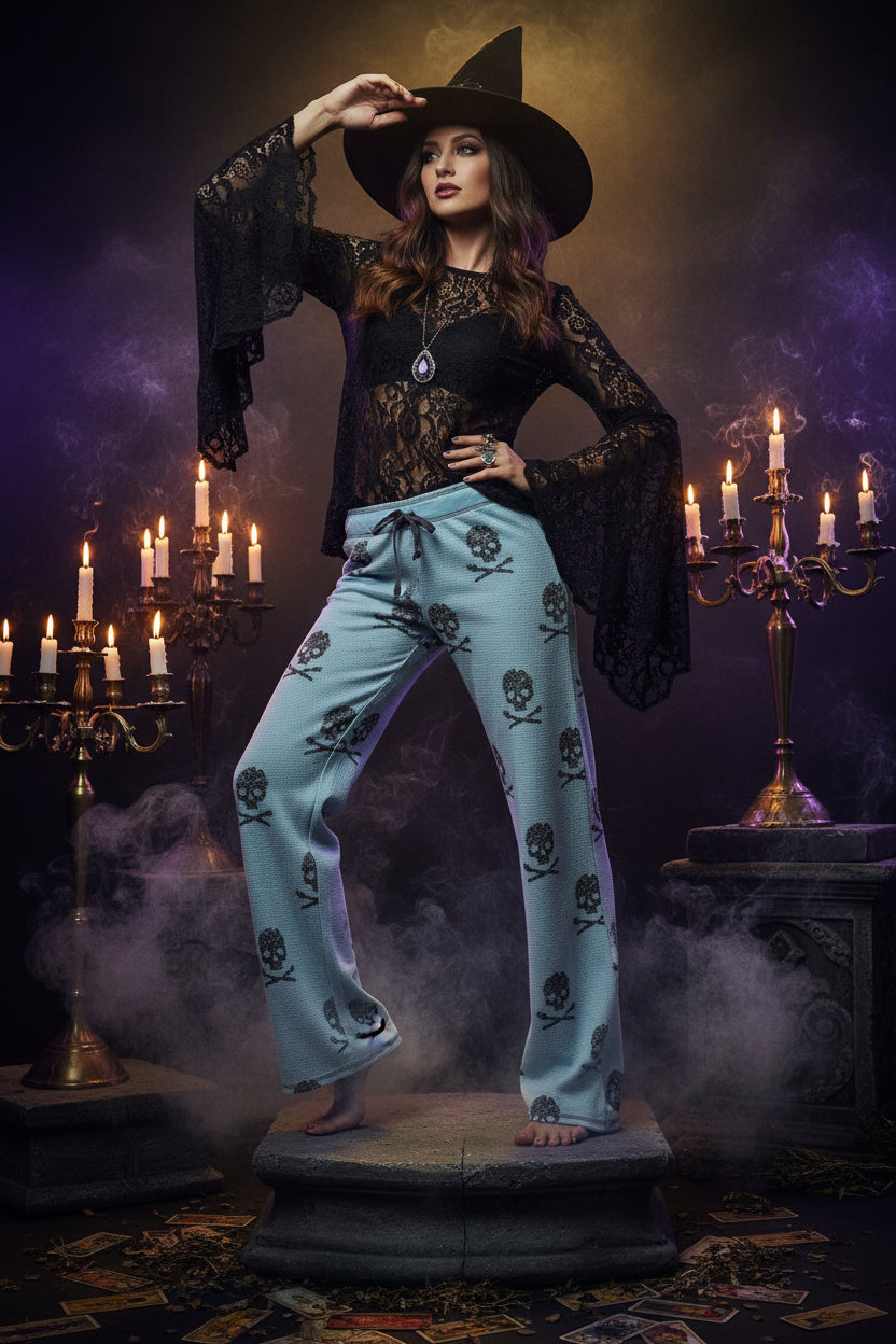 Light blue knit lounge pants with a black skull and crossbones pattern, shown on a model from the waist down against a gray studio background.