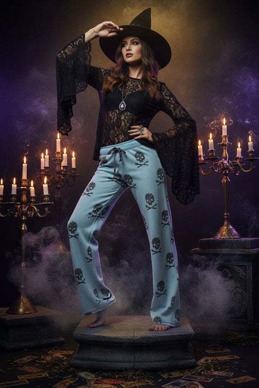 Light blue knit lounge pants with a black skull and crossbones pattern, shown on a model from the waist down against a gray studio background.