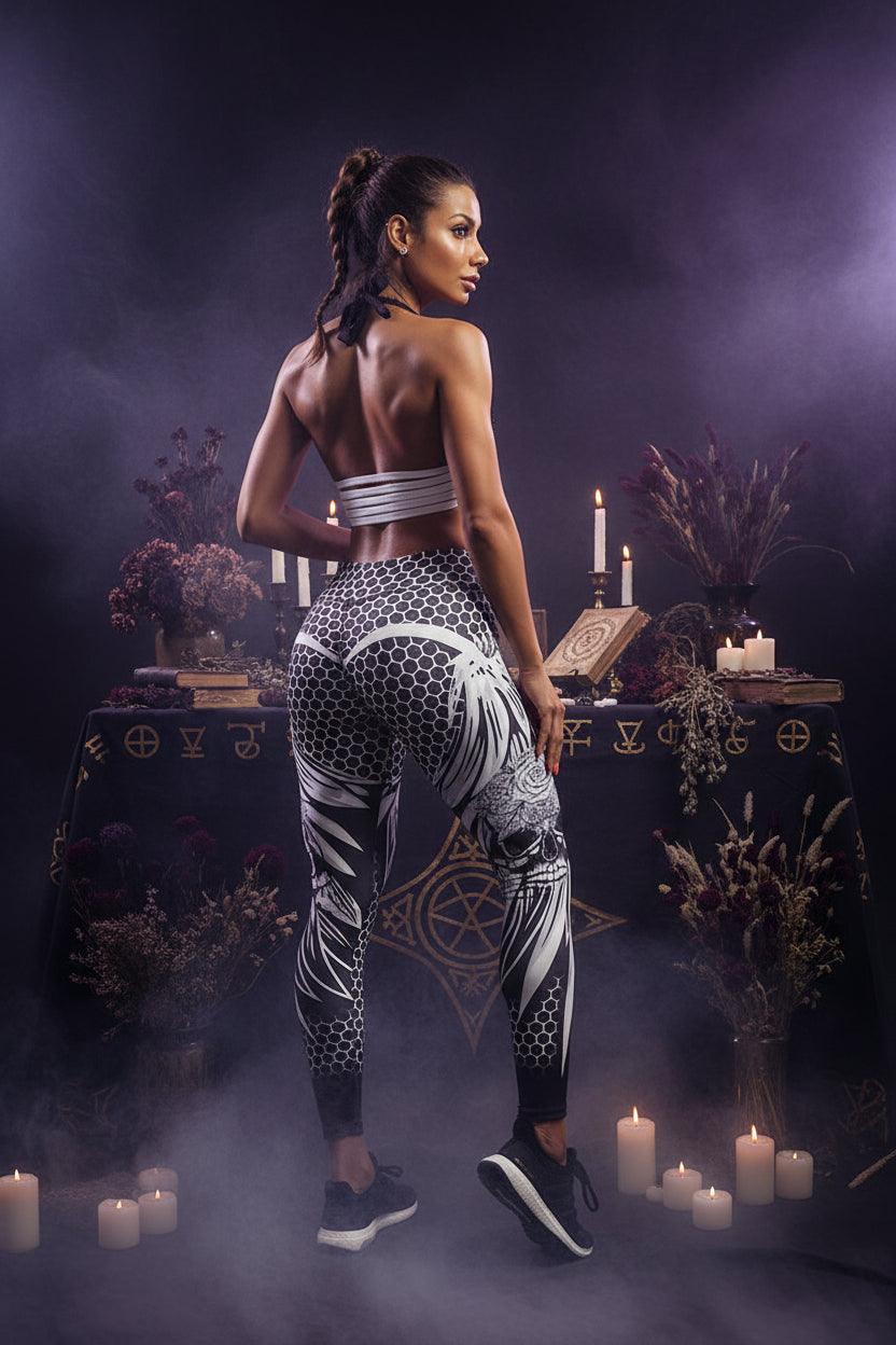 A woman modeling high-waisted athletic leggings with a black, white, and gray floral and geometric pattern, paired with a matching striped sports bra, against a plain white studio background.