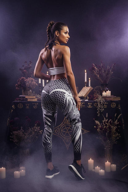 A woman modeling high-waisted athletic leggings with a black, white, and gray floral and geometric pattern, paired with a matching striped sports bra, against a plain white studio background.