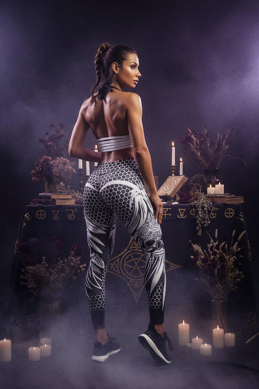 A woman modeling high-waisted athletic leggings with a black, white, and gray floral and geometric pattern, paired with a matching striped sports bra, against a plain white studio background.