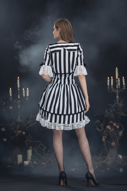 A woman shown from the back wearing a black and white vertically striped dress with white lace ruffle trim at the sleeves and hem, paired with black fishnet stockings and black heels, against a light gray studio background.