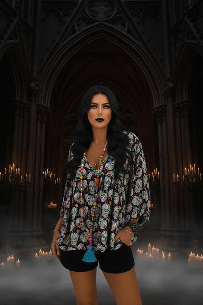 Person wearing a colorful skull patterned top with tassels in front of a decorative wall.
