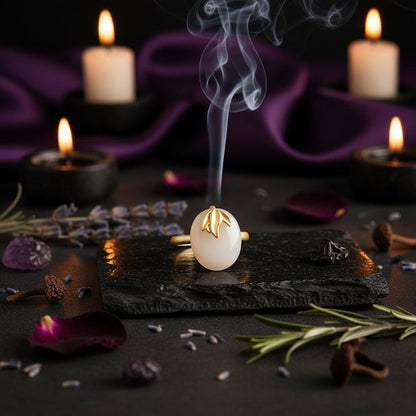 A gold ring with a smooth, oval-shaped white stone and a small leaf detail, resting against a dark wooden block on a textured brown surface.