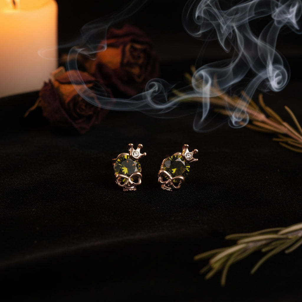 Skull-shaped earrings with green gemstones and rose gold accents on a white background