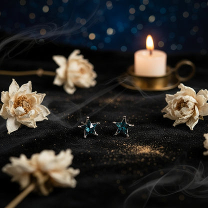 A pair of silver star-shaped stud earrings with iridescent blue-green gemstones, resting on a split beige and white background.