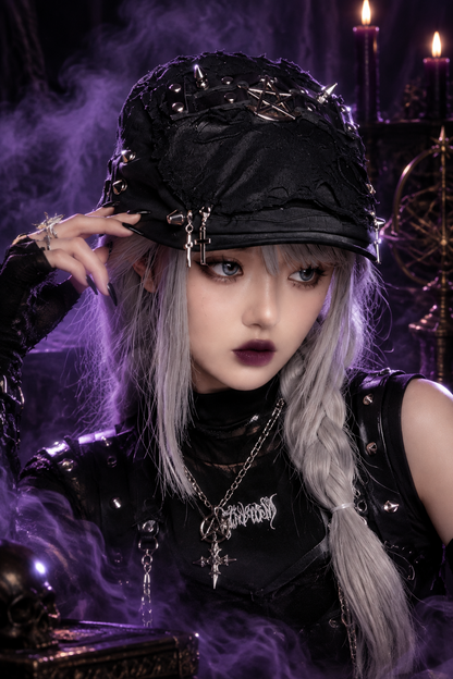 A person wearing a distressed black bucket hat with metal studs, spikes, and a small black pentagram design on the front, paired with a black top and long silver-gray hair, against a plain light background.