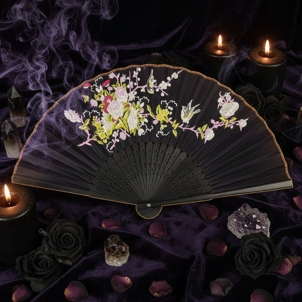 Black folding fan with floral and bird design on a white tray with pink flowers.