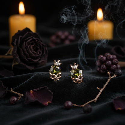 A pair of rose gold stud earrings featuring a central faceted olive green gemstone, adorned with small crown details and tiny clear accent stones, shown on a plain white background.