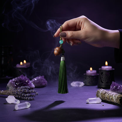 A close-up of a hand holding a traditional Chinese tassel keychain or amulet. The keychain features a green silk tassel, a silver metal cap, a dark green bead, a light blue bead, and two small wooden beads.