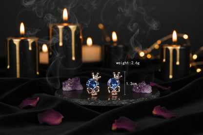 Skull-shaped earrings with blue gemstones and rose gold accents on a white background.