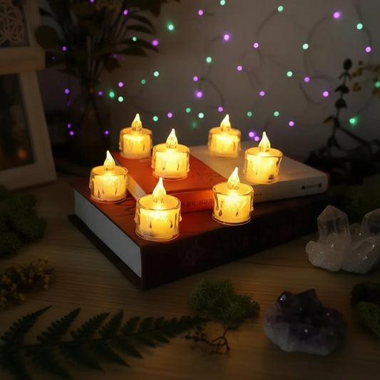 Six small flameless LED tea light candles with a dripping wax design, arranged on top of two stacked books in a warm, dimly lit setting.