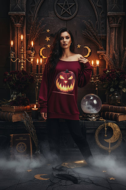 A women's off-the-shoulder long-sleeve sweatshirt in burgundy, featuring a large graphic print of a glowing jack-o'-lantern pumpkin on the front.
