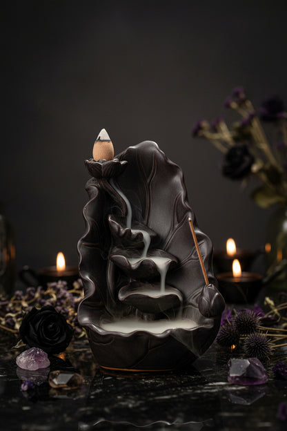 Black ceramic incense burner shaped like a leaf with an incense stick on a wooden surface.